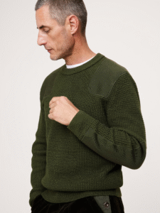 A man with a thick dark green sweater looking at the ground.